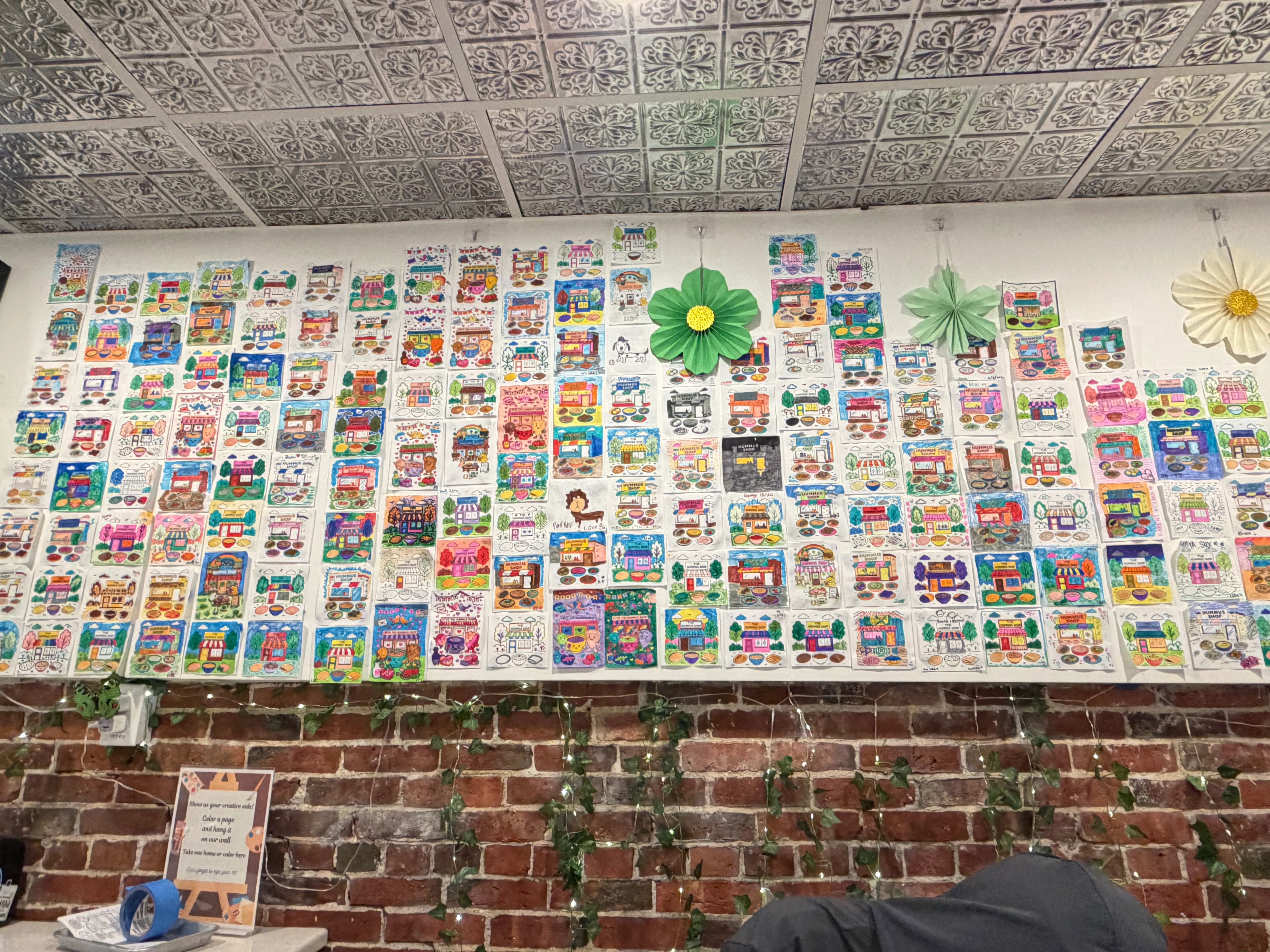 Restaurant wall covered with hundreds of customers' colored-in house drawings above an ivy-laced brick wall